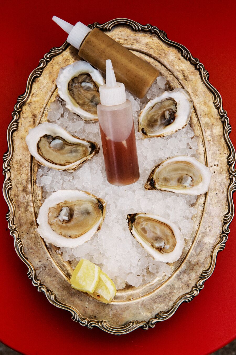 Six oysters on the half shell over crushed ice on a silver tray, with lemon wedges and two squeeze bottles of sauce
