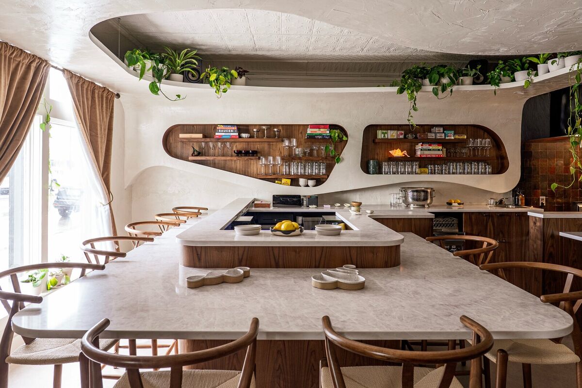 Umbo's dining room — a curved plaster ceiling with trailing plants, wavy walnut shelving of bottles and glassware, and a marble bar lined with wishbone chairs